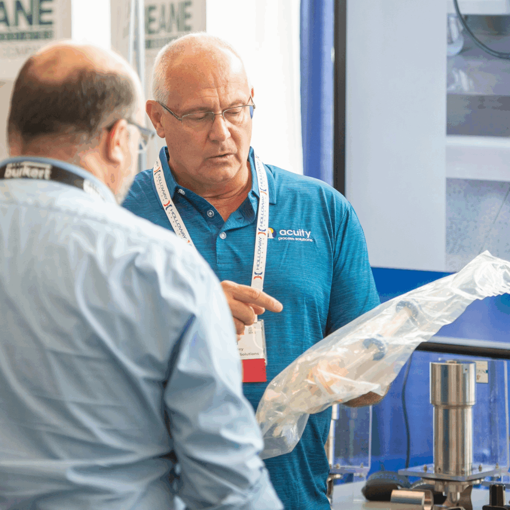 Ted Haley, VP of Sales at Acuity Process Solutions, holding single use tubing assembly and talking to customer at ISPE Boston trade show